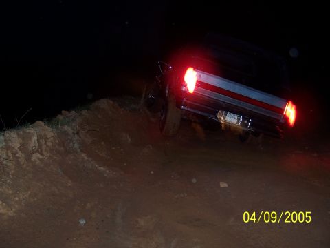 1979 Ford F-150 - Truck driving off-road at night, rear view with taillights on.
