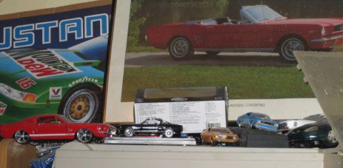 1968 Ford Mustang - A display of toy cars, including a red Mustang and a black coupe, are arranged in front of posters cars.