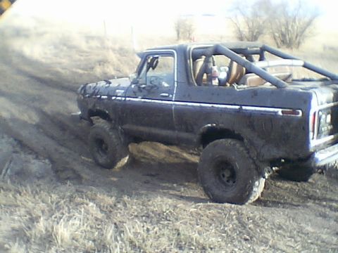 1979 Ford Bronco - This dark SUV with a roll cage navigates a muddy, off-road path.