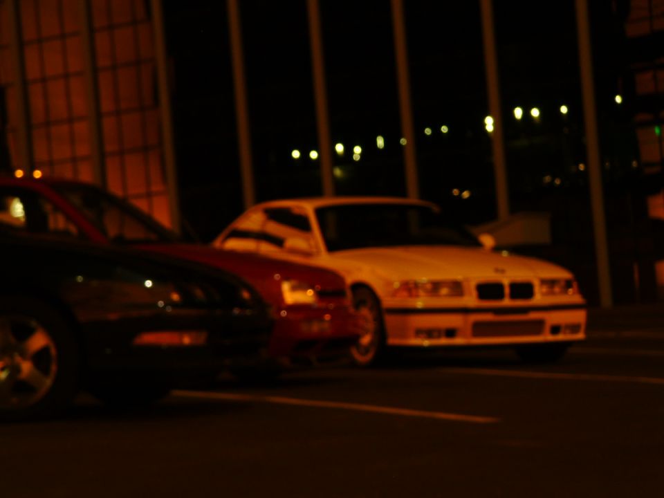 White BMW E36 coupe parked at night next to a red car