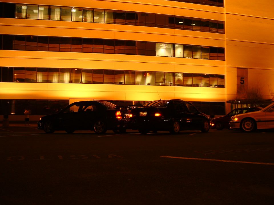 Three sedans parked in front of a lit building at night