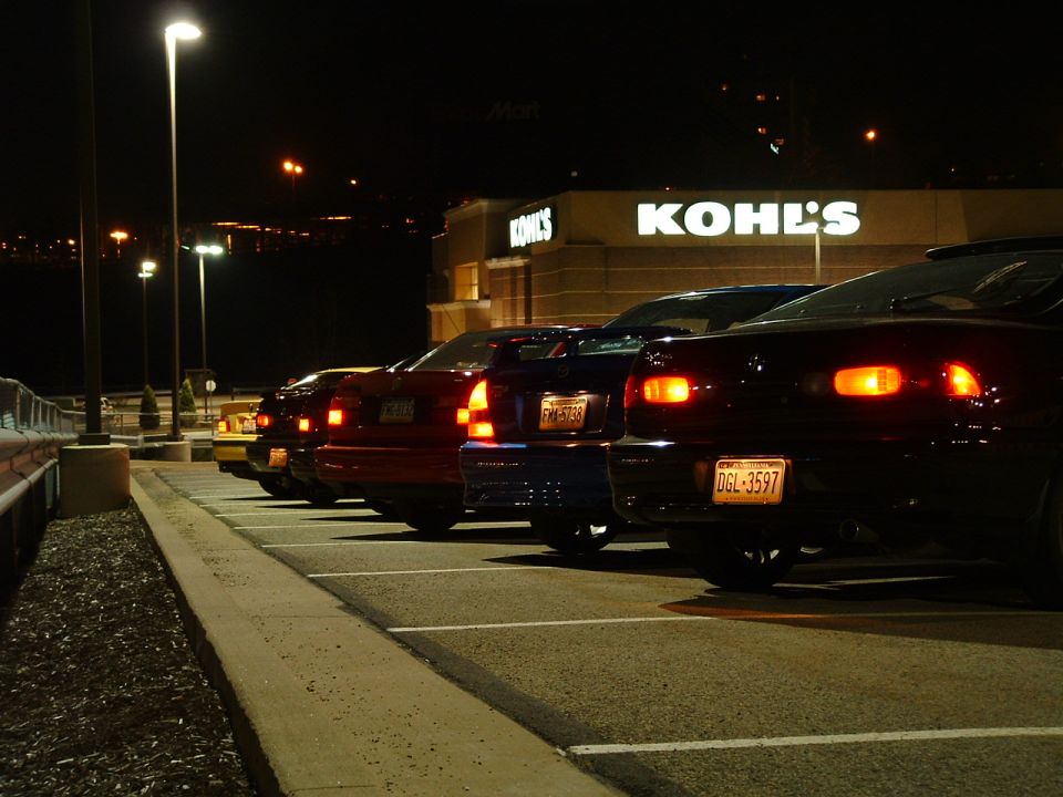 Several cars parked in a lot at night, with Kohl's store in the background. License plates are visible