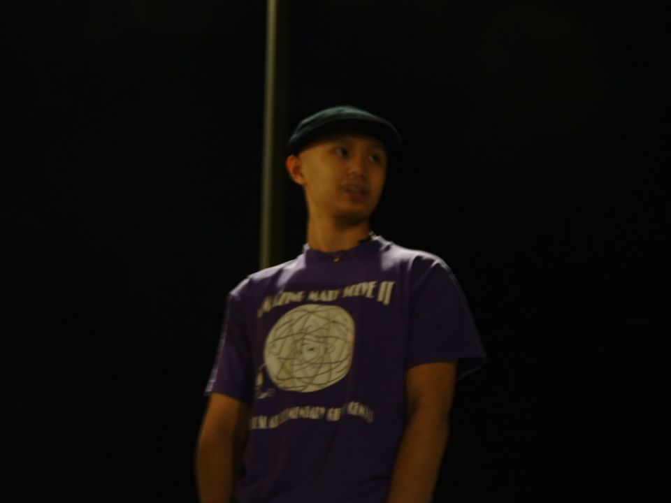 Person in dark cap and purple graphic t-shirt standing at night; no vehicle visible