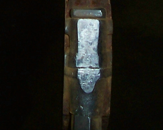 Close-up of a rusty stamped metal component with a number visible on a dark background