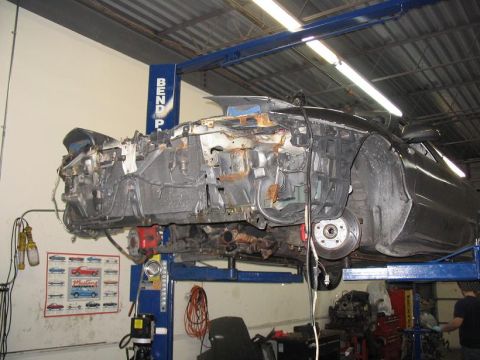 1993 Ford Probe - A heavily damaged car is suspended on a lift in a repair shop, revealing its rusted internal components.
