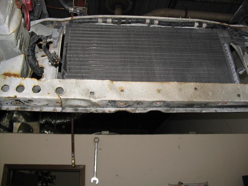 Close-up of a car's radiator and surrounding metal support structure, showing rust and some wiring