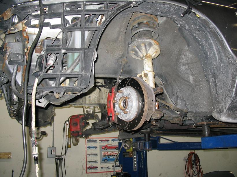 Front wheel well and suspension with red brake caliper and perforated rotor