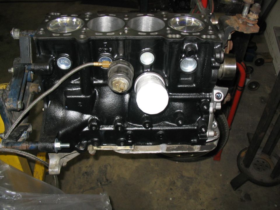 black engine block with oil filter and various sensors attached, resting on a stand
