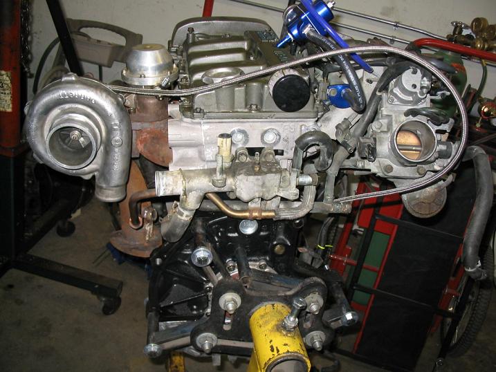 Turbocharged engine assembly on a stand, showing intake manifold, turbocharger, and exhaust manifold