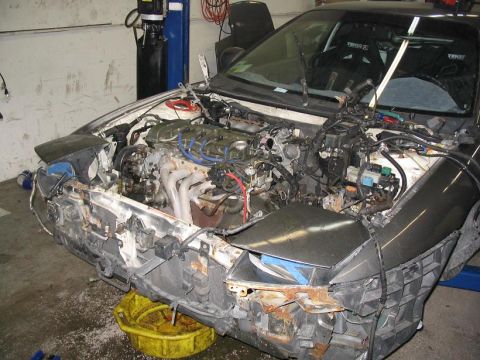 1993 Ford Probe - The front end of a car is disassembled, revealing the engine and various components. An oil drain pan sits below.