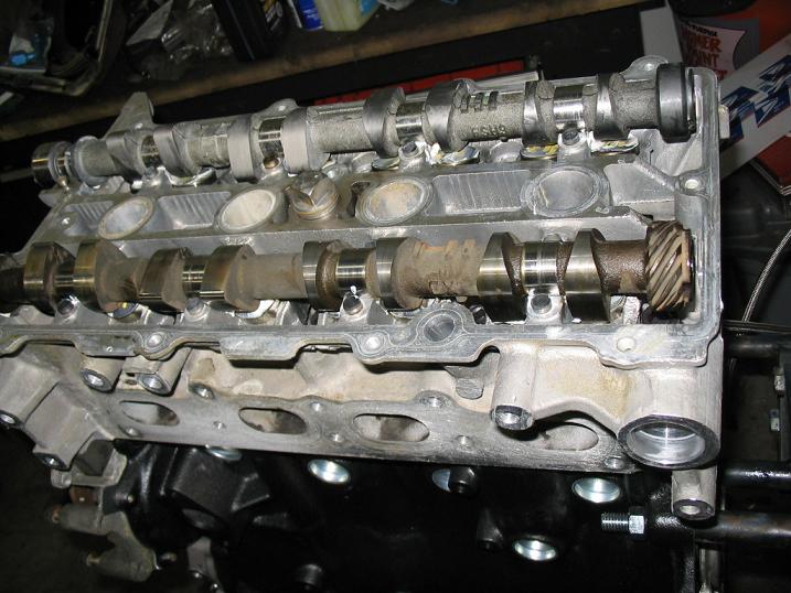 Engine cylinder head with dual camshafts, one showing wear. Visible text includes 'F5H9' and a Supermotors.net watermark