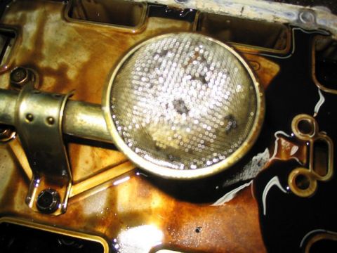 1993 Ford Probe - Close-up of a dirty oil strainer and pan, showing metallic debris and dark oil.