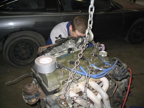 1993 Ford Probe - Mechanic attends to an engine suspended by chains, with a dark-colored car visible in the background.