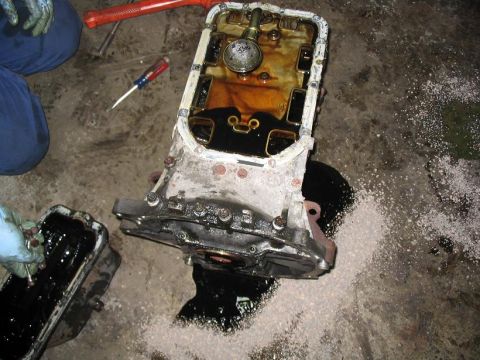 1993 Ford Probe - A mechanic works on an engine oil pan, revealing its internal components and dark oil.