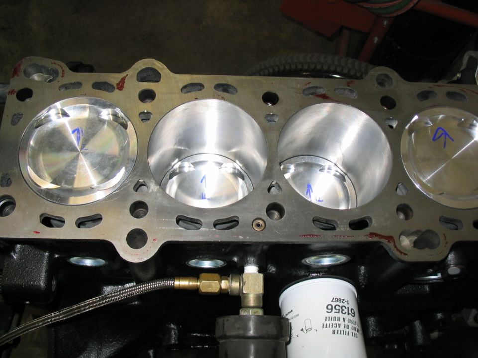 Engine block with four cylinders and pistons, showing blue markings on pistons. Oil filter visible below