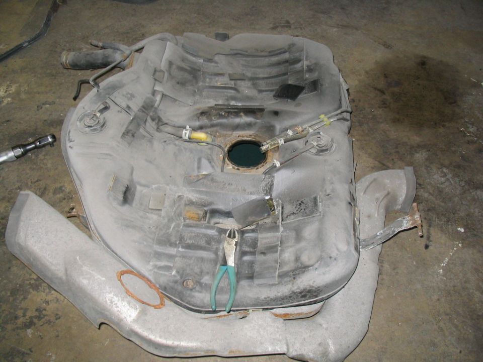 Removed fuel tank with pliers and a socket wrench on a concrete floor