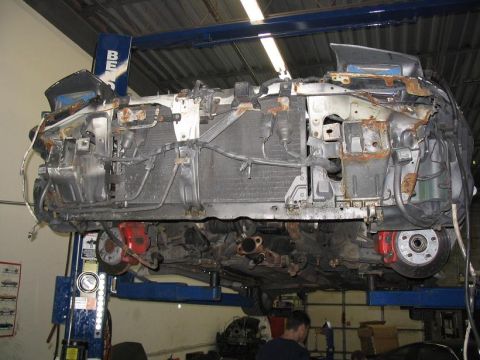 1993 Ford Probe - The front end of a vehicle is shown from underneath while on a lift, revealing extensive damage and rust.