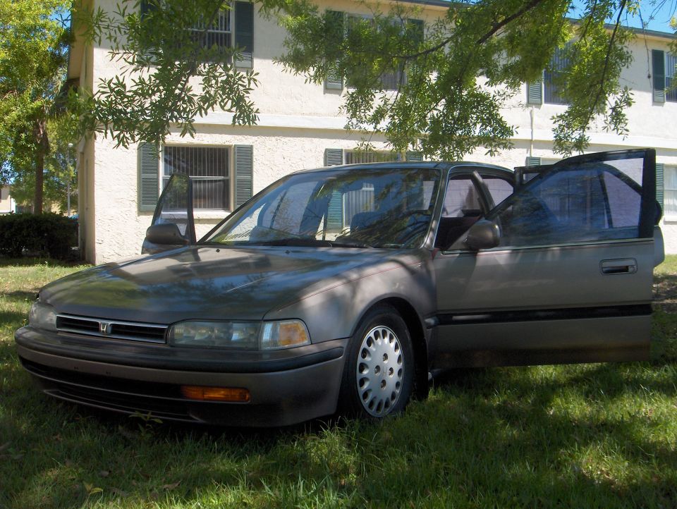Gray Honda Accord sedan with driver-side doors open, parked on grass by an apartment building