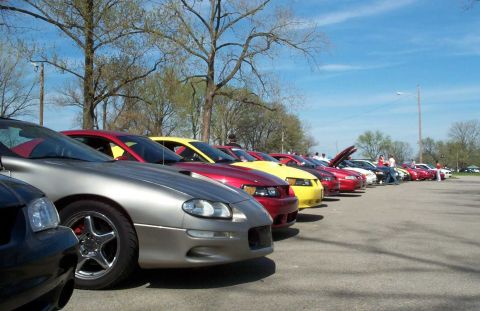 1998 Ford Crown Victoria - A row of cars, including a silver Camaro and several Mustangs, are parked at an outdoor event under a clear blue sky.