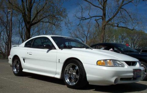 1998 Ford Crown Victoria - White 1996 Ford Mustang coupe with chrome wheels parked outdoors.