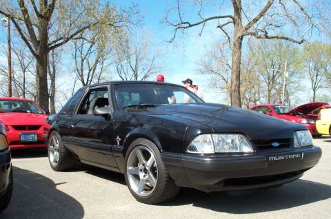 1998 Ford Crown Victoria - A black Ford Mustang is parked at an outdoor car show with other vehicles visible.