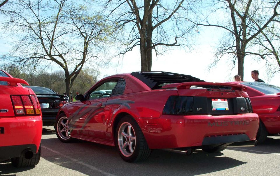 Red Mustang coupe with flame graphics, window louvers and spoiler at a car show