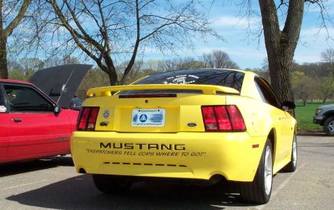 1998 Ford Crown Victoria - A yellow Ford Mustang is parked at an outdoor event, with another car visible to its left.