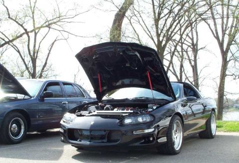 1998 Ford Crown Victoria - A black sports car with its hood open is parked next to a dark sedan, both with hoods up.