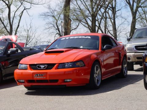 1998 Ford Crown Victoria - An orange Ford Mustang is parked at an outdoor event with other vehicles visible.