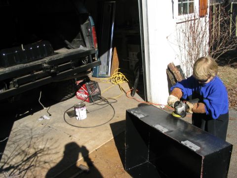 1986 Ford Bronco - A person grinds a custom fuel tank in a garage, with the rear of a Ford Bronco visible.