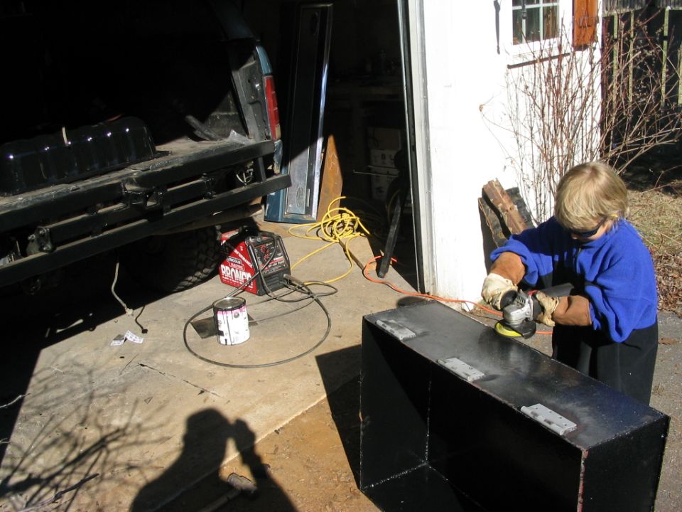 Person grinding a custom fuel tank next to a Ford Bronco's rear
