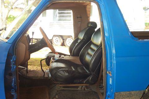 1987 Ford Bronco - Interior of a blue truck with aftermarket seats, trailer visible outside.