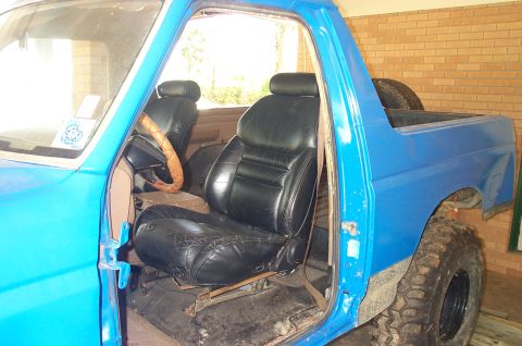 1987 Ford Bronco - The interior of a blue pickup truck shows worn black leather seats and a tan steering wheel.