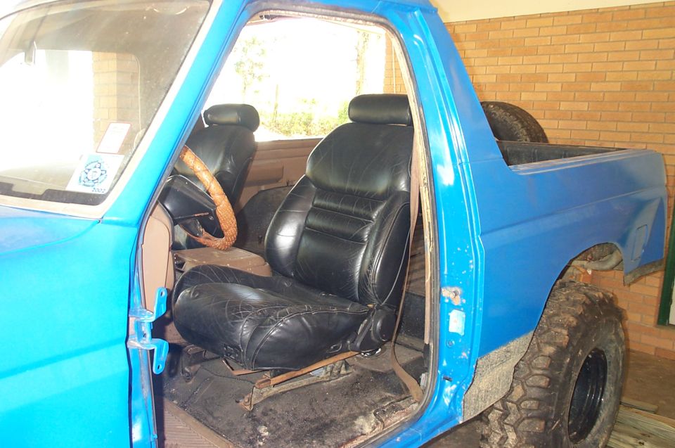 Blue pickup truck interior with black leather seats and a tan steering wheel. The driver's side door is open