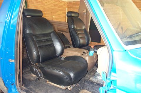 1987 Ford Bronco - The interior of a blue vehicle displays aftermarket black leather seats and a center console.