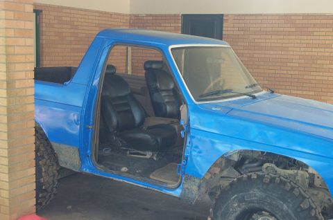 1987 Ford Bronco - The interior of a blue 1987 Ford Bronco is visible, black bucket seats and an open driver's side door.