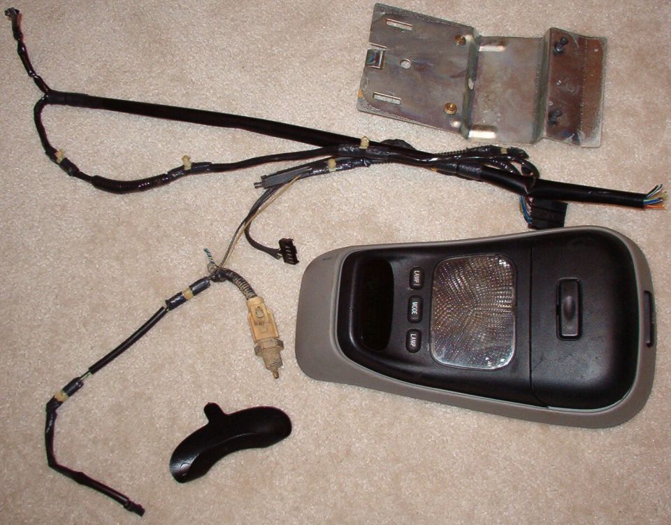 Disassembled overhead console, wiring harness, mounting bracket and shifter handle laid on carpet