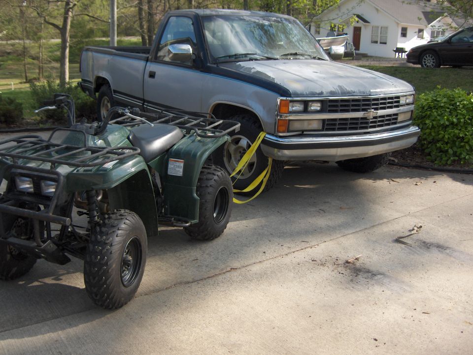 Two-tone 1988-98 Chevrolet pickup towing a green ATV on a trailer in a driveway