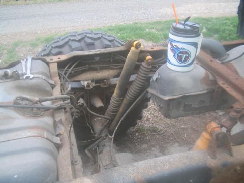 1983 Ford F-250 - The rear frame of a truck is visible, with a fuel tank, shocks, and a tire. A mug with a sports logo is placed on the tank.