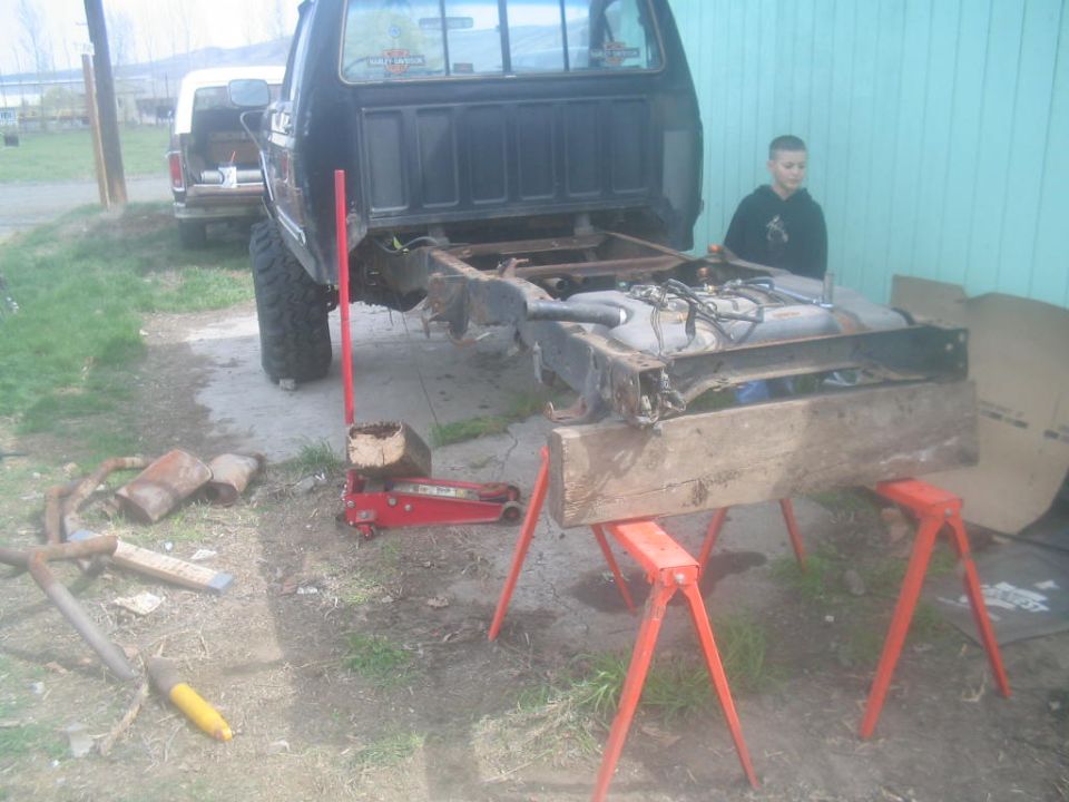 Truck bed removed, frame and fuel tank on sawhorses, another truck in background
