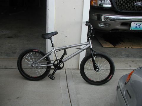 1998 Jeep TJ - A silver BMX bicycle is parked in front of a garage, with a Ford truck partially visible in the background.