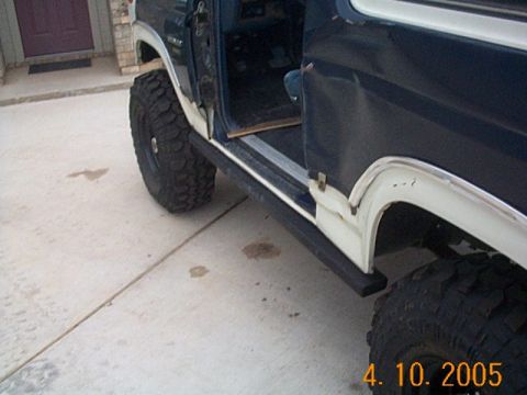 1986 Ford Bronco - This dark blue SUV features white trim and aggressive tires, with visible running boards and an open driver's door.