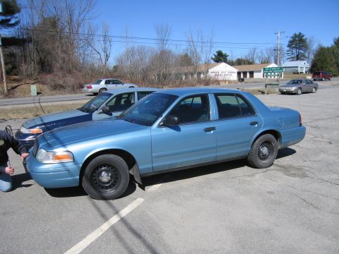 1991 Ford LTD Crown Victoria - A blue sedan is parked in a lot with other vehicles visible in the background under a clear blue sky.