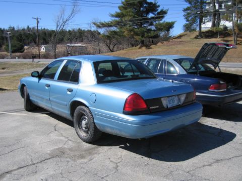 1991 Ford LTD Crown Victoria - Two blue sedans are parked outdoors on a sunny day, one with its trunk open.