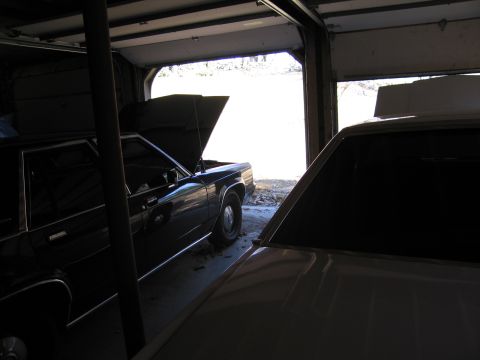 1991 Ford LTD Crown Victoria - Two vehicles are parked inside a garage with the main garage door open.