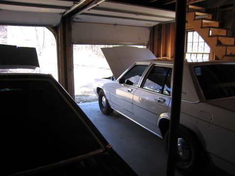 1991 Ford LTD Crown Victoria - A white sedan sits in a garage with its hood open, partially obscured by another vehicle.