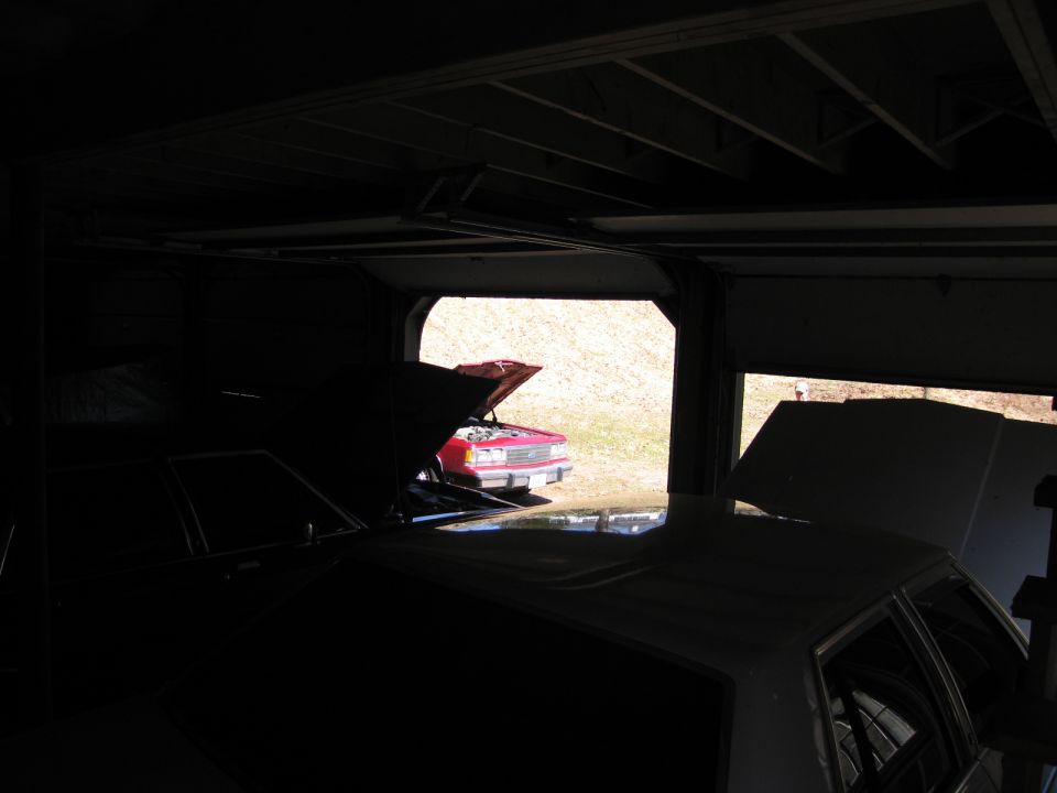 Red sedan with hood open, parked outside a garage. Front view shows grille and headlights