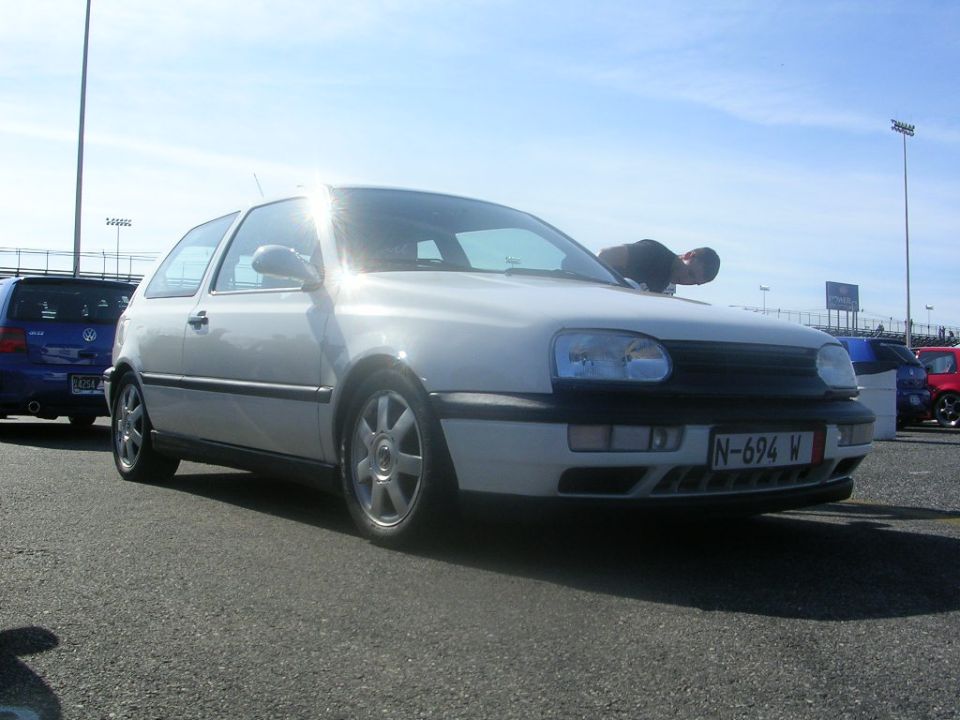 White VW Golf Mk3 with a person leaning over the hood, parked next to a blue VW Golf. License plate N-694 W is visible