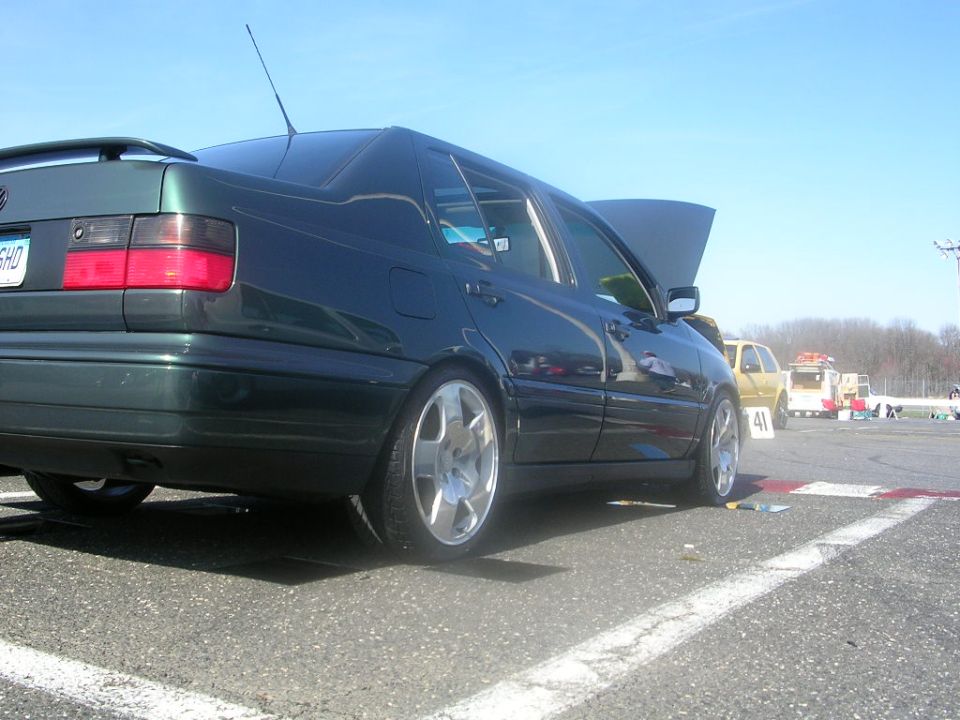 dark green sedan with hood up, parked on asphalt with white lines, other cars and trees in background