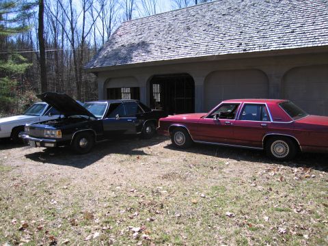 1991 Ford LTD Crown Victoria - Three sedans, including a red 1991 Ford Crown Victoria LTD, are parked outside a garage.